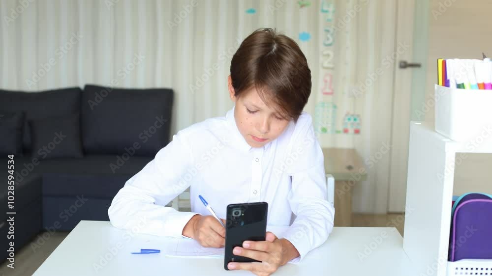 a teenage boy is sitting comfortably at a desk, working on his homework while using his mobile phone. Teenager with mobile phone in hands indoors a teenage boy is sitting comfortably at a desk, working on his homework while using his mobile phone. Teenager with mobile phone in hands indoors