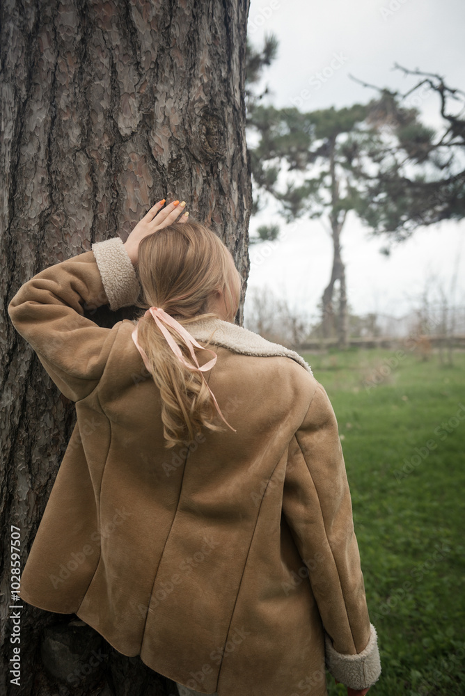 person in the forest. The girl stands near the tree. Touches the trunk of the pine. Looks into the distance. Wears a warm jacket. In the forest among the trees in spring. person in the forest. The girl stands near the tree. Touches the trunk of the pine. Looks into the distance. Wears a warm jacket. In the forest among the trees in spring.