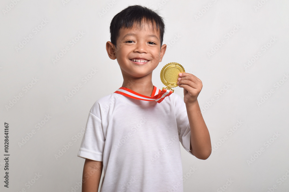 Little Asian boy smiling happily holding a gold medal on his chest isolated on a white background. The boy celebrating his victory Little Asian boy smiling happily holding a gold medal on his chest isolated on a white background. The boy celebrating his victory