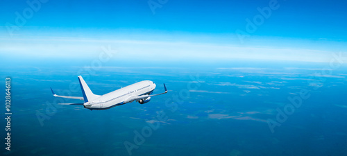 Airplane flying in the sky over the sea, travel panoramic background with modern white airplane flying high over the ground. Flying airplane with blank white livery