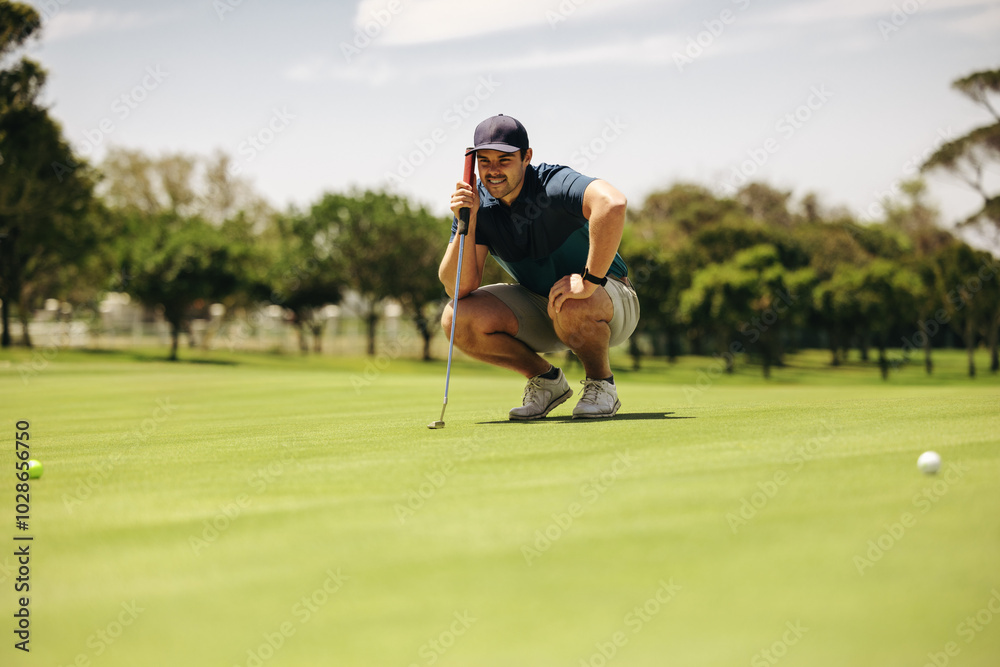 Caucasian man crouching and aiming on putting green, focusing on golf ball with a golf club in hand Caucasian man crouching and aiming on putting green, focusing on golf ball with a golf club in hand