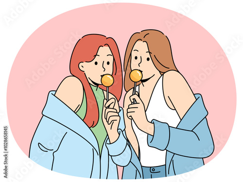 Two women with chupa chups in hands dressed in fashionable seductive clothes eat lollipops. Lovely girls in stylish jackets slung off shoulders to advertise new candies for teenagers