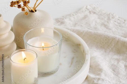 Cozy still life composition with aroma candles, vase with dry flowers on the marble tray on the table. Home interior decoration, copy space.