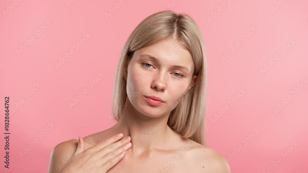 Young blonde woman posing at camera, touches neck and collarbone smooth skin, isolated on pink studio background. Beauty skin care concept Young blonde woman posing at camera, touches neck and collarbone smooth skin, isolated on pink studio background. Beauty skin care concept