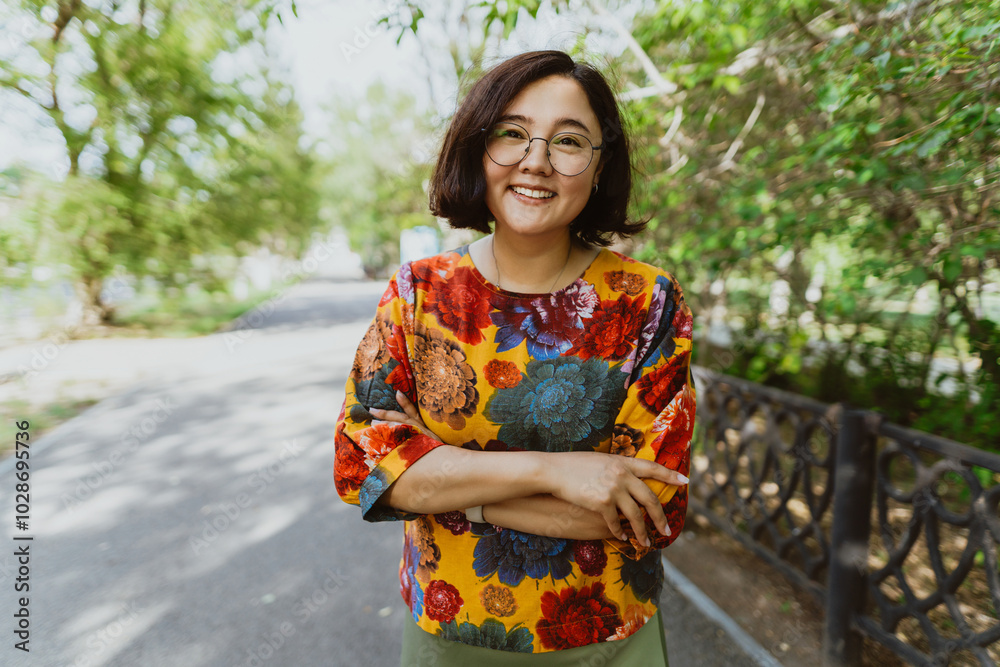 Joyful young Asian woman with crossed arms enjoying a sunny day in the park. A smiling woman with crossed arms stands in a lush park and radiates happiness Joyful young Asian woman with crossed arms enjoying a sunny day in the park. A smiling woman with crossed arms stands in a lush park and radiates happiness