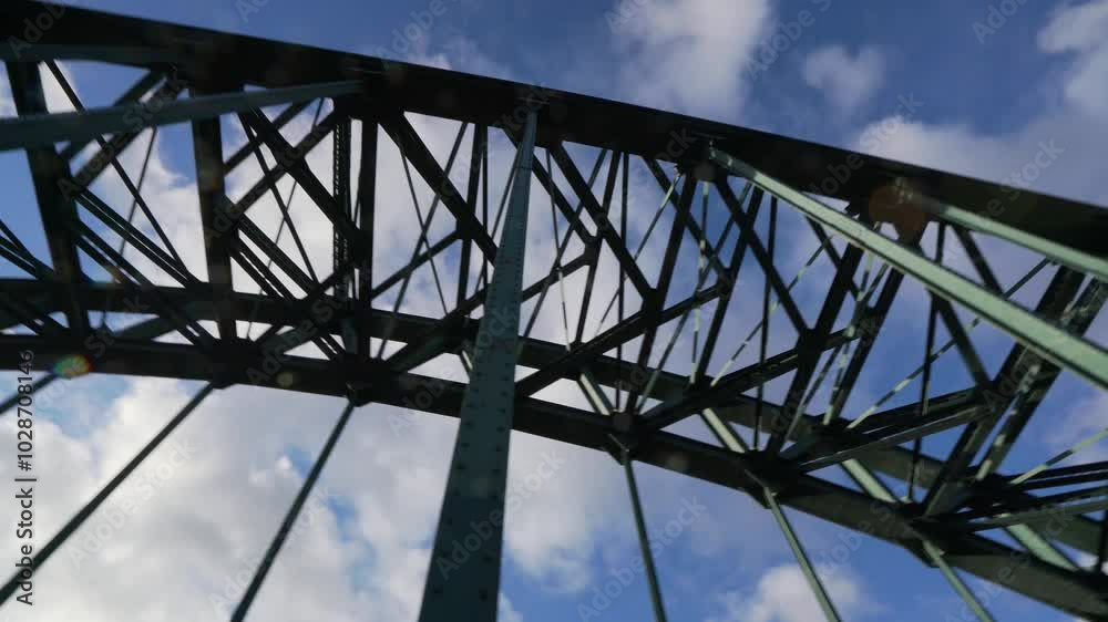 Steel bridge structure against a blue sky with clouds, shot from below, showcasing its framework Steel bridge structure against a blue sky with clouds, shot from below, showcasing its framework