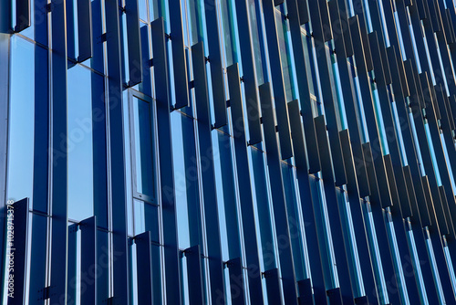 Close-up of modern glass building facade with geometric patterns reflecting sky. Contemporary architectural design.