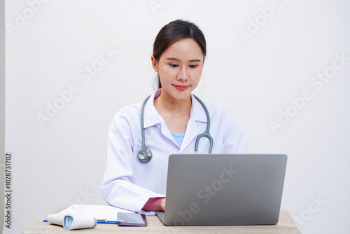 A female doctor works on a laptop in an examination room.