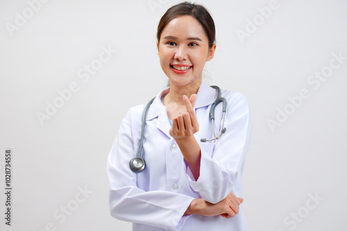 Smiling Asian female doctor puts a stethoscope on her shoulder. Wearing a white lab coat standing holding a note board on gray background.