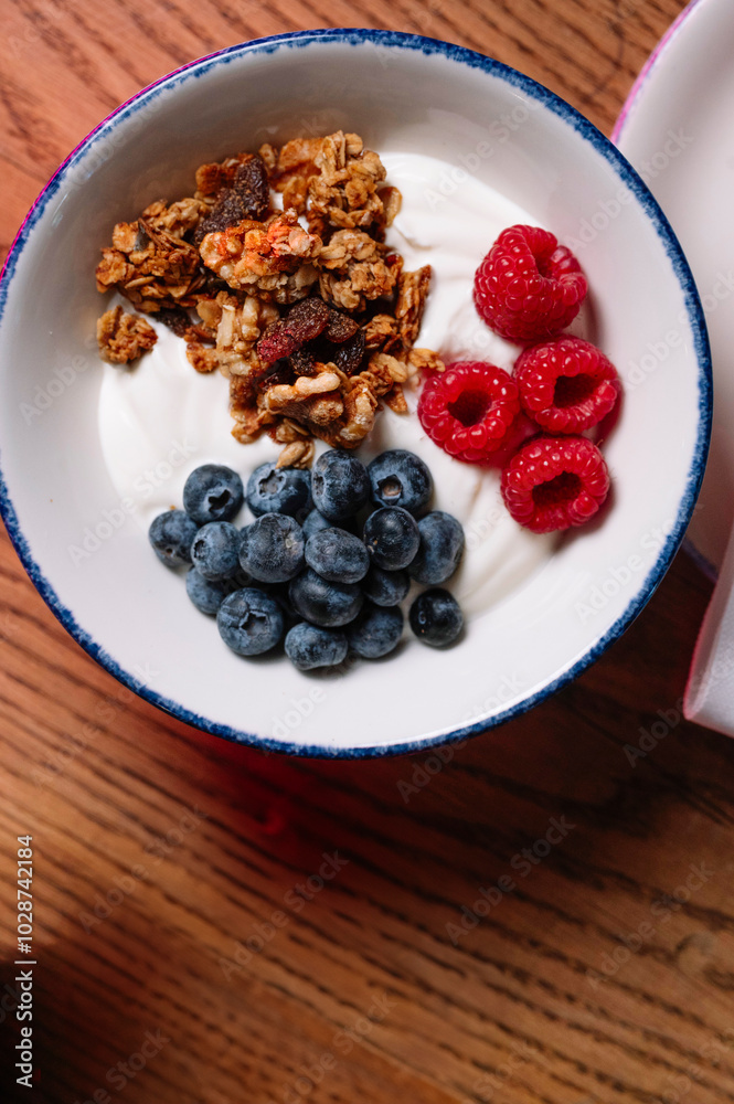 A bowl of yogurt parfait with granola, raspberries, and blueberries.