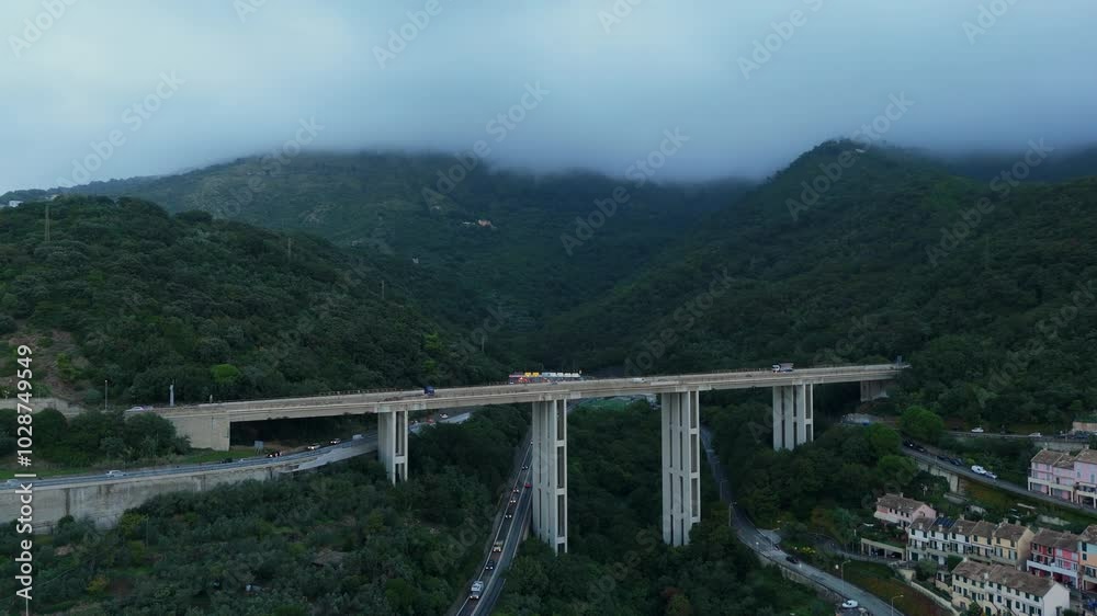 Cars travel across a high bridge between green mountains on a cloudy day Cars travel across a high bridge between green mountains on a cloudy day