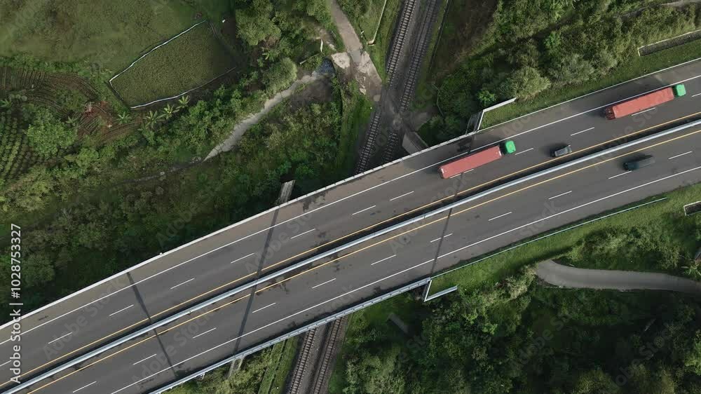drone video of large vehicles passing on a highway with train tracks underneath, the drone stays close to the object and the camera faces downwards
