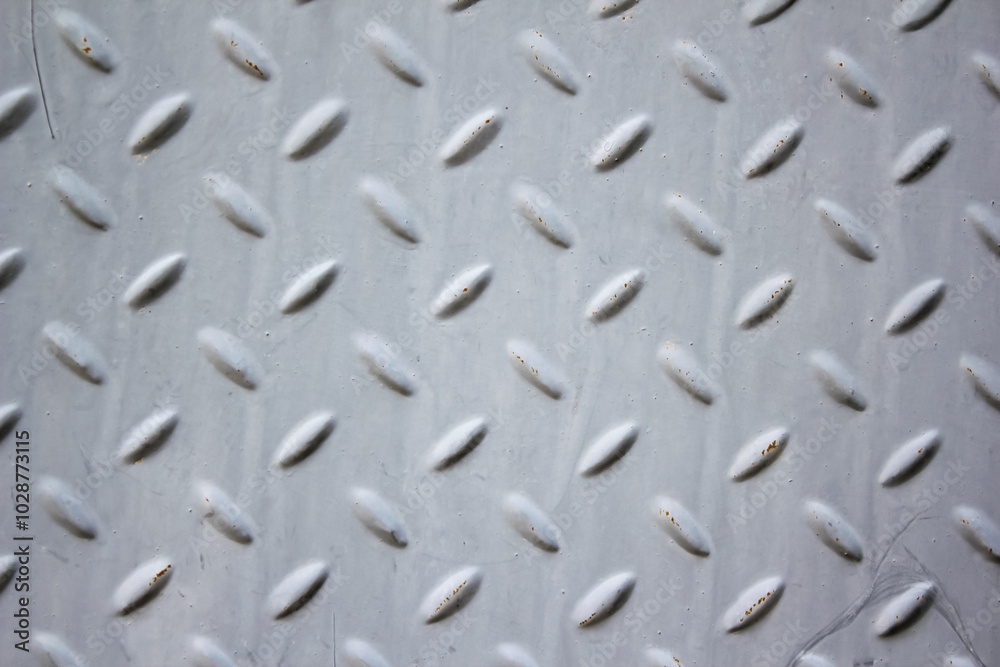 A close-up of a metal surface with a diamond plate pattern. The metal is painted gray, but there is a patch of rust at the bottom edge. A close-up of a metal surface with a diamond plate pattern. The metal is painted gray, but there is a patch of rust at the bottom edge.