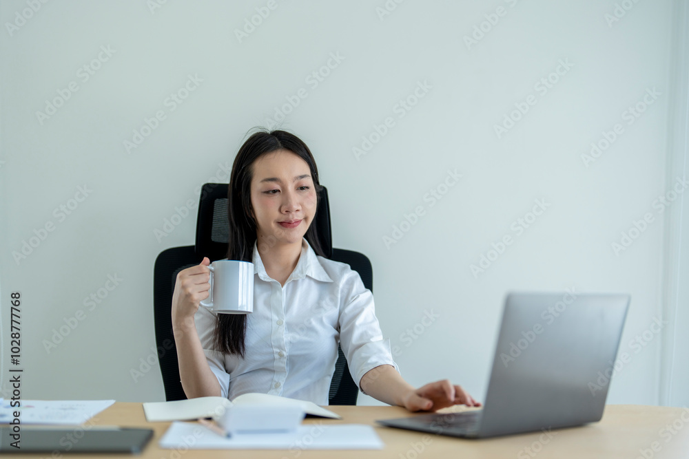 Young asian businesswoman drinking coffee working on laptop in office Young asian businesswoman drinking coffee working on laptop in office