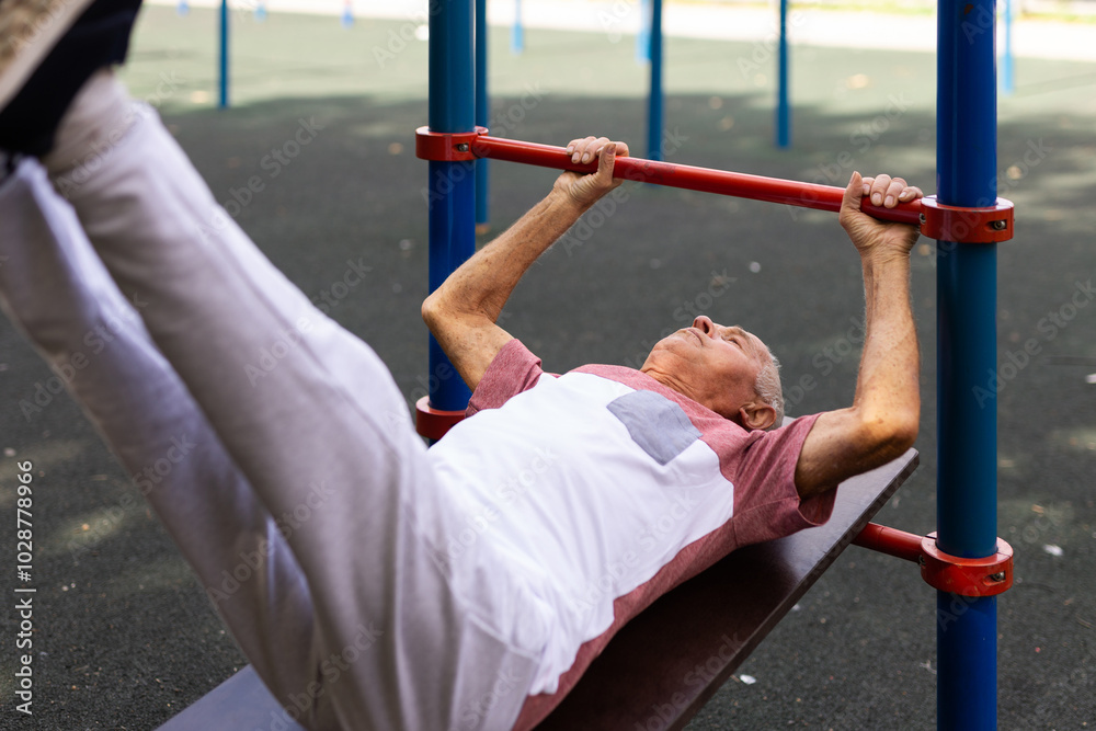Obraz premium Open air gym. Street training on the municipal sports equipment. Elderly man pumps the press in city park