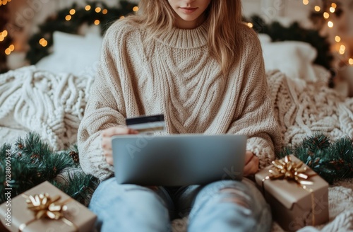 Young woman wearing a sweater sits on a bed surrounded by Christmas trees and...