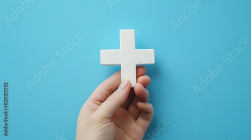 A hand holding a white cross against a blue background.