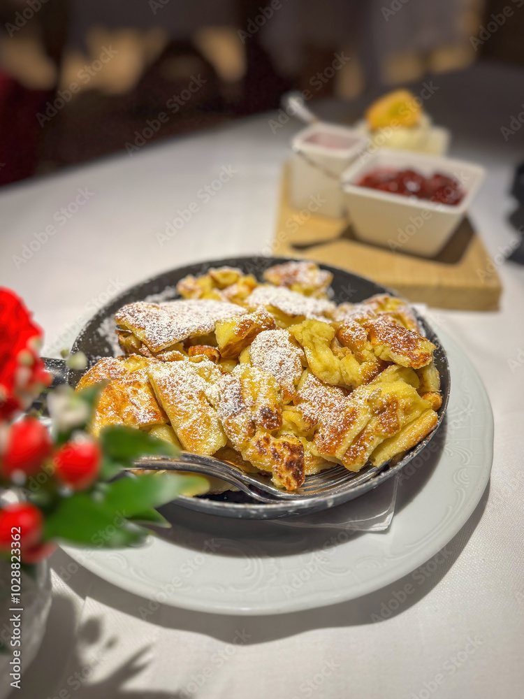 Famous Austrian sweet dish Kaiserschmarrn served in a pan with ice cream, raspberry and stewed plums