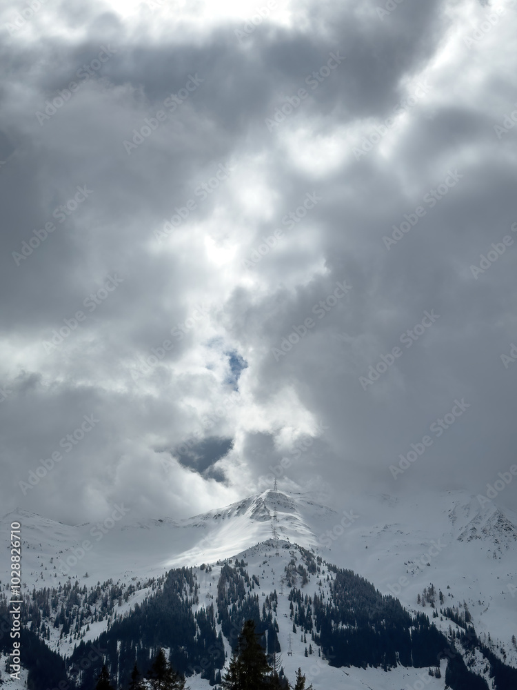Electric power line runnnig up a snow covered mountain with snow line at the bottom in the ski region of Saalbach-Hinterglemm, Austria against dramatic cloudy sky