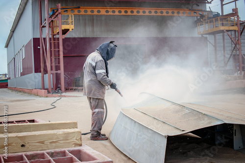 Bilde på lerret Worker performing sandblasting on a metal structure to eliminate rust at an indu
