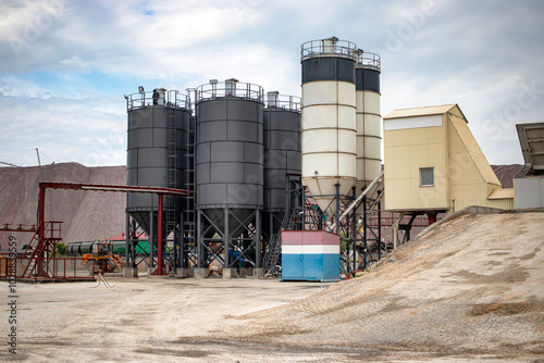 Industrial concrete plant with cement bins and batchers in operation during daytime under a cloudy sky photo