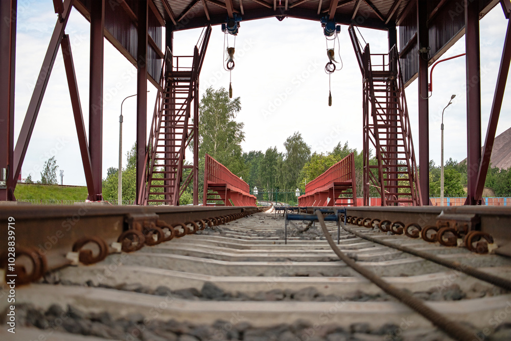 Loading and unloading platform for railway cars at an industrial site, featuring cranes and stairs under a clear sky Loading and unloading platform for railway cars at an industrial site, featuring cranes and stairs under a clear sky