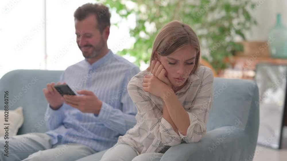 Stressed Wife Sitting aside on Sofa while Relaxed Husband Using Phone Stressed Wife Sitting aside on Sofa while Relaxed Husband Using Phone