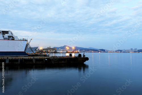 Busan International Cruise Terminal, Busan Port, Jung-gu, Busan, Korea - August 26, 2019: Night view of a man who is fishing near a bug cruise ship.  photo