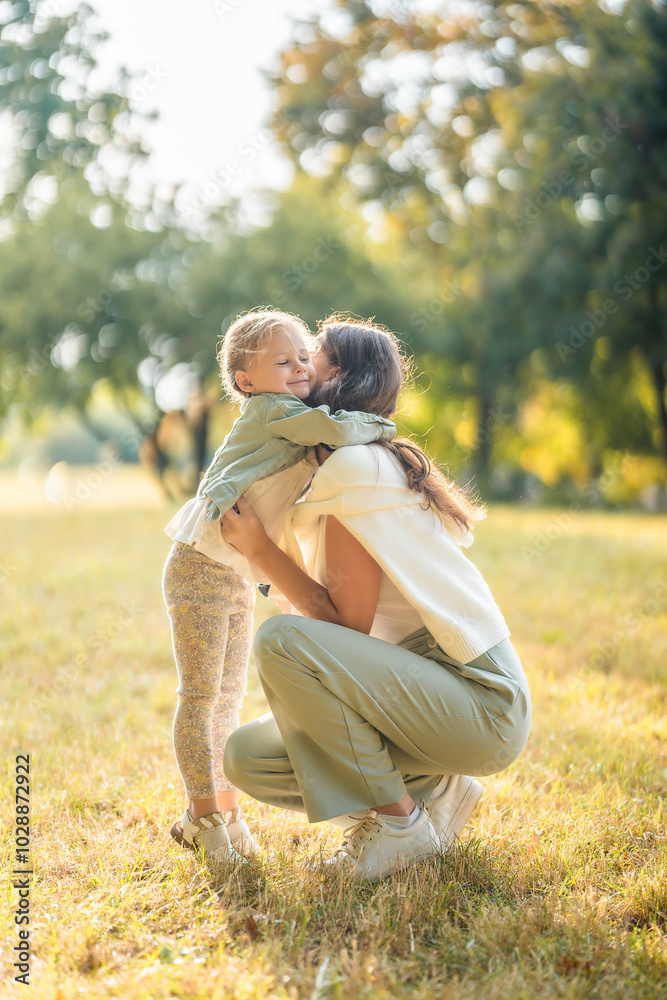 Fototapeta premium Young mother and little daughter hugging and playing together in autumn park in Prague, Europe