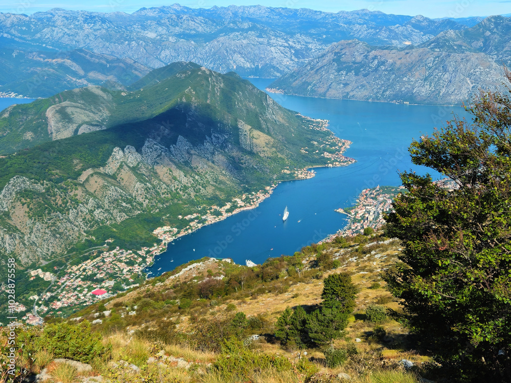 Horizontal aerial view of the Bay of Kotor in Montenegro, surrounded by mountains, coastal towns, and blue water, with copy space in the sky. Ideal for travel promotions or social media backgrounds.
