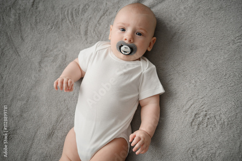 Cute infant lying comfortably on back on cozy blanket with pacifier in mouth, peacefully resting in this position, top view. Concept maternity leave, child care, infancy photo