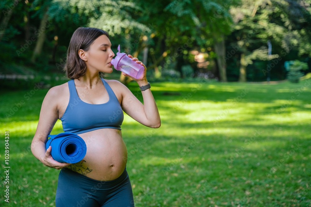 Pregnant woman practicing yoga during summer day drinking water from bottle Pregnant woman practicing yoga during summer day drinking water from bottle