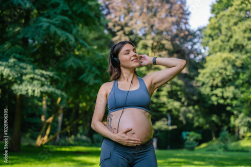 Pregnant woman with headphones listening music during yoga workout in park