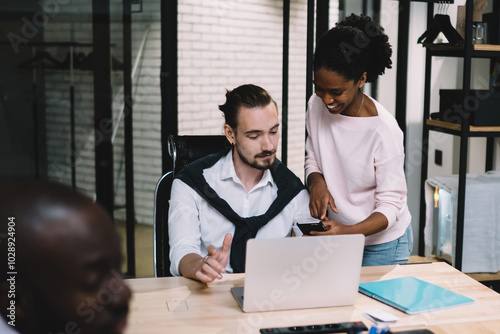 Multicultural group of professional employees in formal wear collaborating on task using modern technology with wireless internet connection during brainstorming meeting in office interior