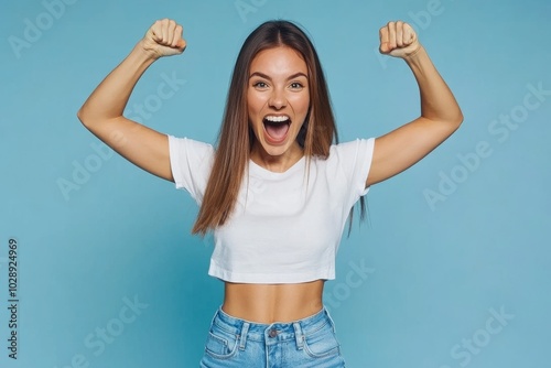 An attractive young woman is seen on a blue colored background winning with her fists while dressed in stylish white clothes