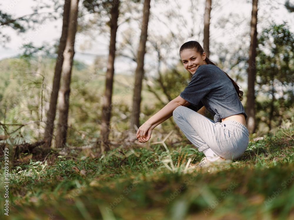 Cheerful young woman squatting on grass in a serene forest, enjoying nature and the outdoors, expressing joy and tranquility Nature and wellness concept Cheerful young woman squatting on grass in a serene forest, enjoying nature and the outdoors, expressing joy and tranquility Nature and wellness concept