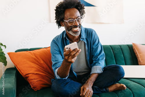 Bilde på lerret Happy mature man relaxing on the sofa, smiling and using a mobile phone
