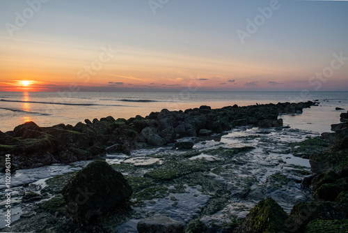 A stunningly beautiful sunset casts a warm glow over the rocky shoreline with serene and tranquil waters nearby