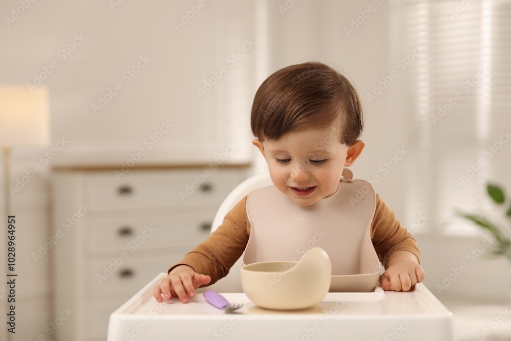 Cute little baby eating healthy food from bowl in high chair at home, space for text Cute little baby eating healthy food from bowl in high chair at home, space for text