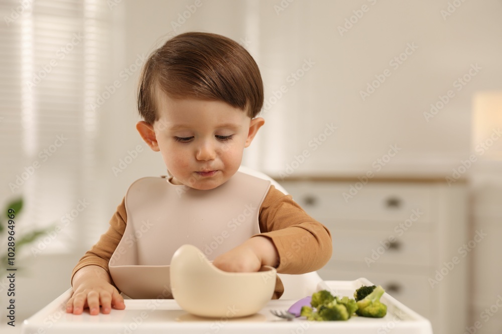 Cute little baby eating healthy food from bowl in high chair at home Cute little baby eating healthy food from bowl in high chair at home