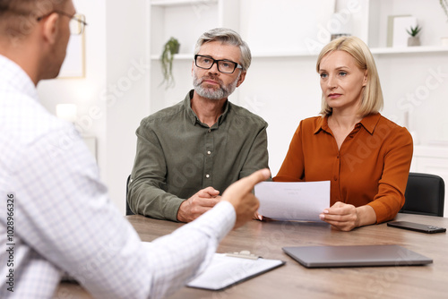 Pension plan. Couple consulting with insurance agent at table indoors