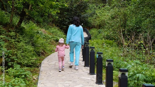 Mom and daughter walk along a path in the park. Mountain landscape. Lots of greenery