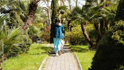 Mom pushing a stroller with a baby in a tropical garden