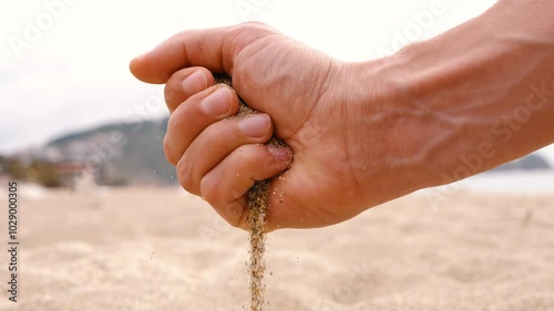 Time slips away like sand through your fingers. Hand pours sand on the beach