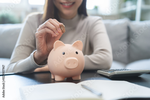 Saving money wealth concept, asian young business woman hand putting coin into piggy for saving cost, cash finance planning to spend enough money on her income for save money, payment tax, investing. photo