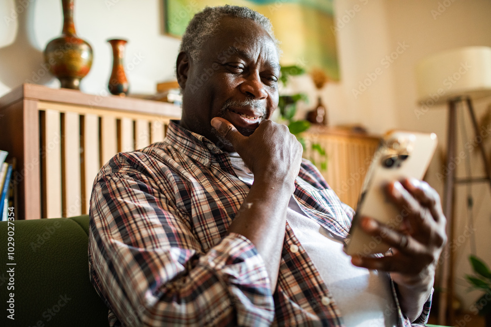 Naklejka premium Close up of a senior black man using smartphone on home sofa