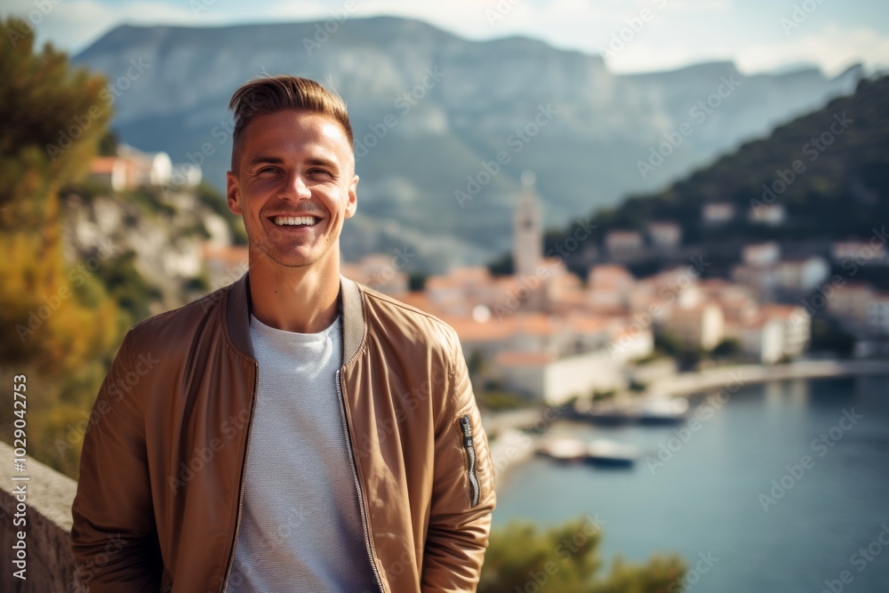 Portrait of a joyful man in his 20s wearing a trendy bomber jacket isolated in picturesque seaside village Portrait of a joyful man in his 20s wearing a trendy bomber jacket isolated in picturesque seaside village