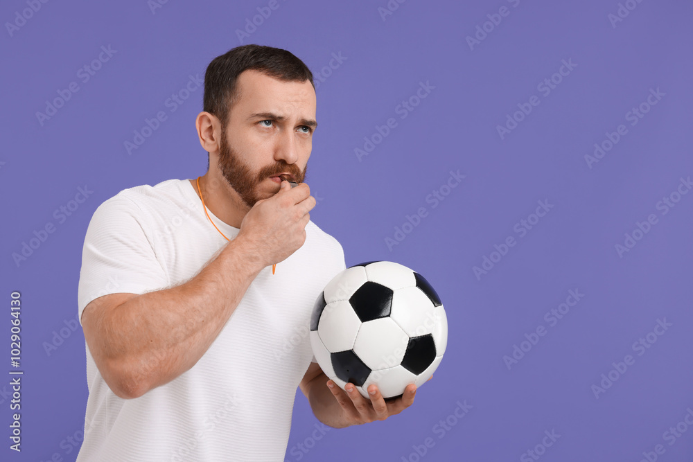 Young man with soccer ball blowing whistle on purple background, space for text Young man with soccer ball blowing whistle on purple background, space for text