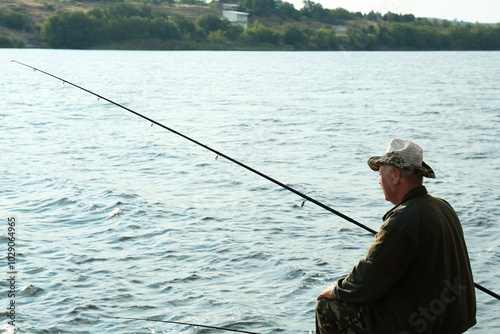 Fisherman with rod fishing near lake at summer