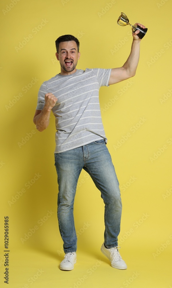 Happy winner with golden trophy cup on yellow background Happy winner with golden trophy cup on yellow background